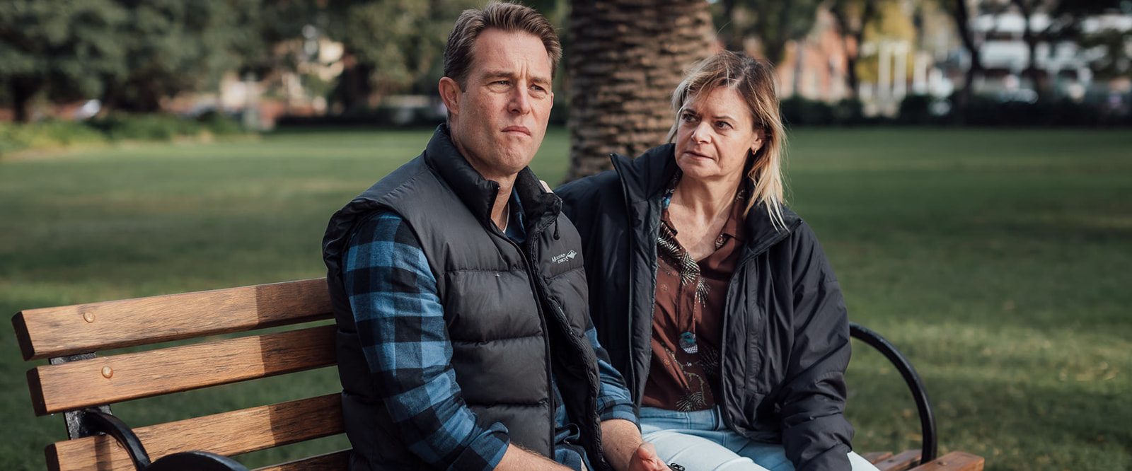 A man and woman sitting on a park bench, having a difficult conversation.