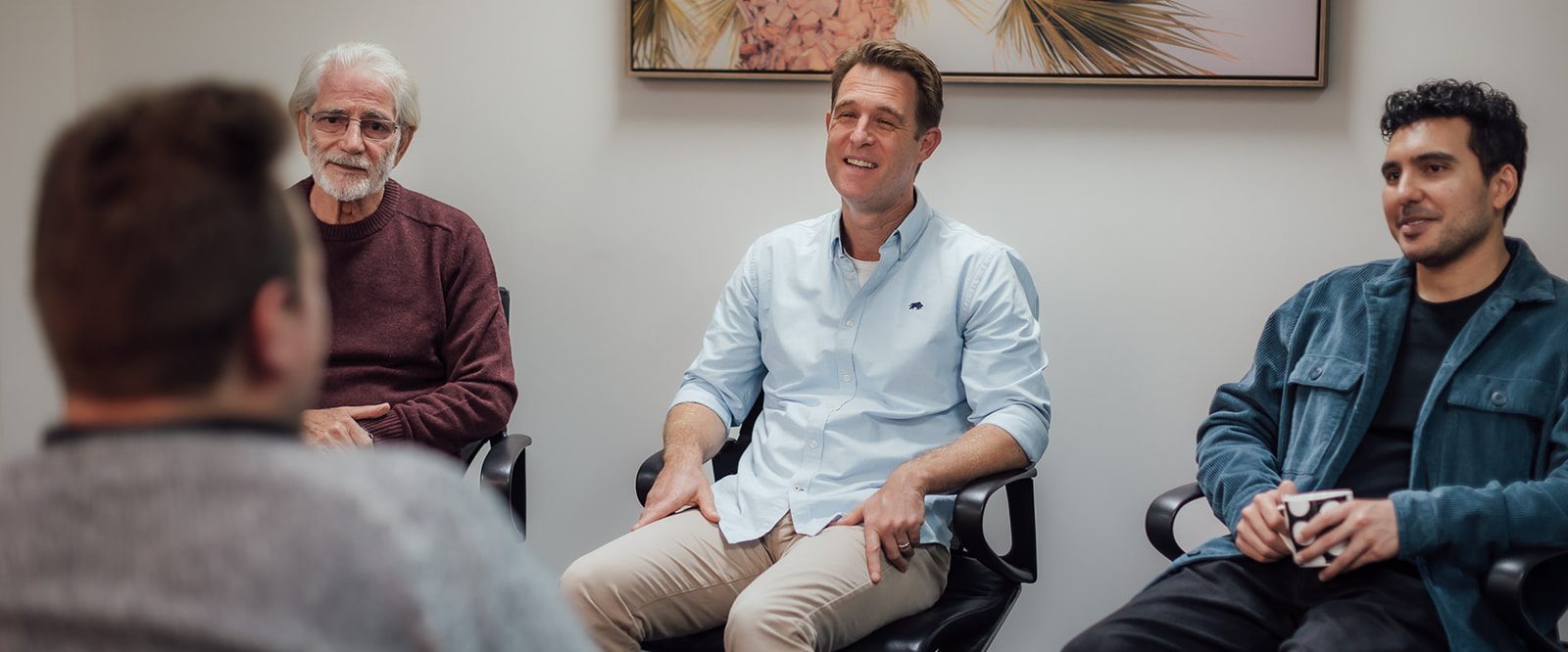 Three men sitting in a group, talking with a male facilitator.