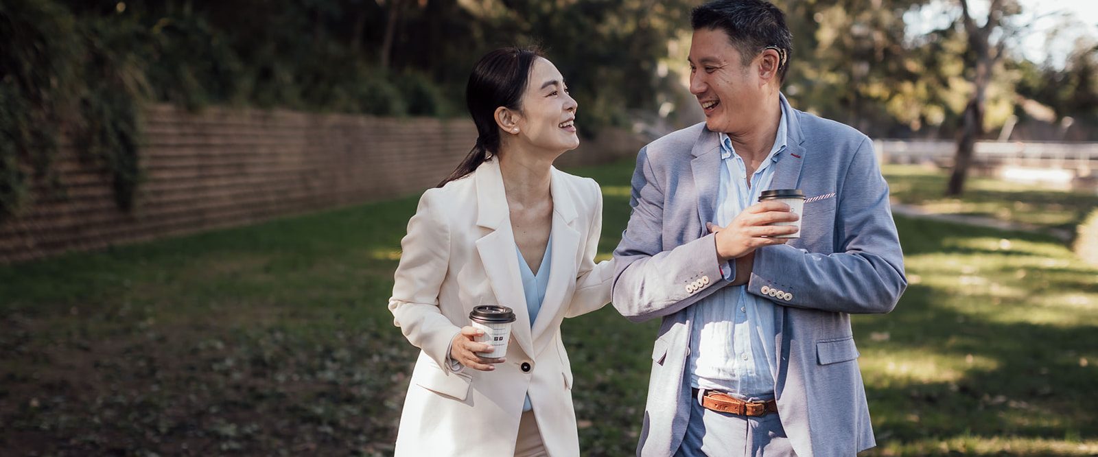 A man with a cochlear implant, laughing and walking in nature with a woman.